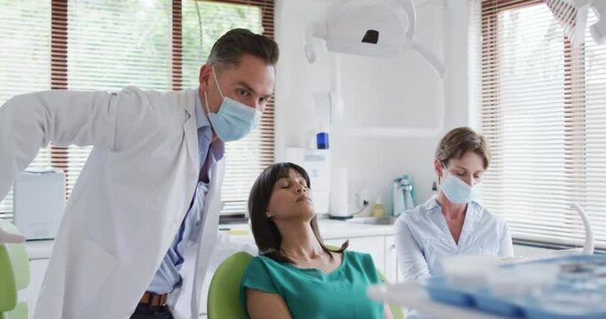 Caucasian male dentist with face mask examining teeth of female patient at modern dental clinic