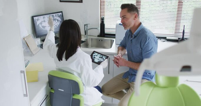 Biracial female dentist with face mask examining teeth of male patient at modern dental clinic