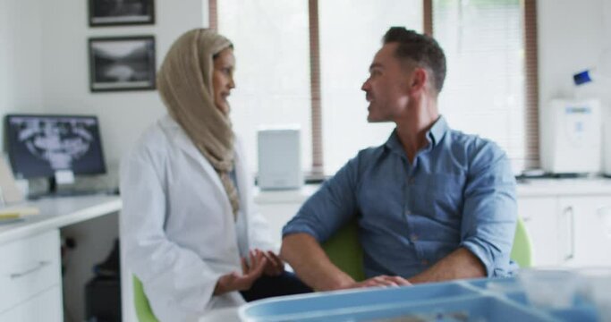 Biracial female dentist talking with male patient at modern dental clinic