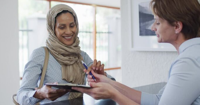Smiling biracial woman talking and signing documents at reception at modern dental clinic