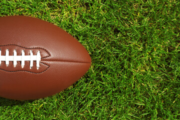 American football ball on green grass, top view. Space for text