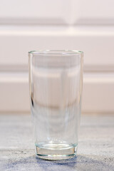 Large empty transparent glass standing on a blue wooden table in the kitchen. A glass of milk for breakfast.