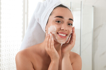 Beautiful young woman applying cleansing foam onto face in bathroom. Skin care cosmetic