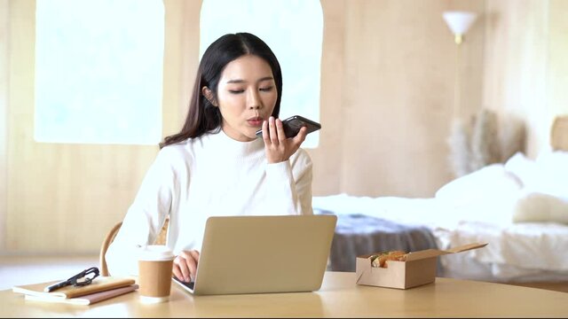 Beautiful smiling Asian creative woman wearing sweater with talking on mobile phone while working at home with laptop computer. Young Asian Freelancer woman work from home. Small Business owner.
