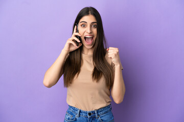 Obraz na płótnie Canvas Young caucasian woman using mobile phone isolated on purple background celebrating a victory in winner position