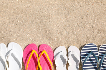 Fototapeta na wymiar Many different flip flops on sand, flat lay. Space for text