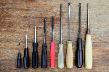Old screwdriver tools of different sizes lie in a row on an old wooden background