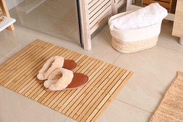 Wooden mat and slippers on tiled floor in bathroom. Stylish accessory