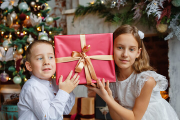 Fototapeta na wymiar The children leaned their heads against the gift. A girl and a boy with gifts under the Christmas tree. Brother and sister are happy with New Year's gifts.