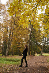 young woman with long hair and dark clothes stands sideways in the autumn forest