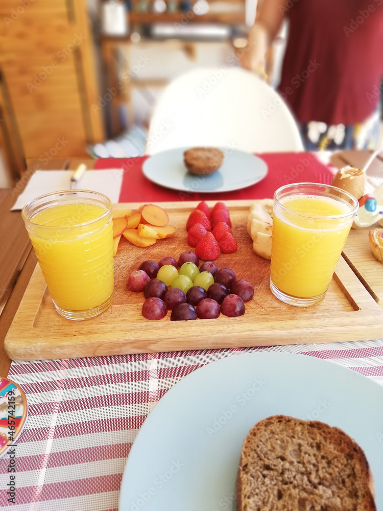 Sticker Vertical shot of a wooden plate with berries and two glasses of orange juice for breakfast at a cafe