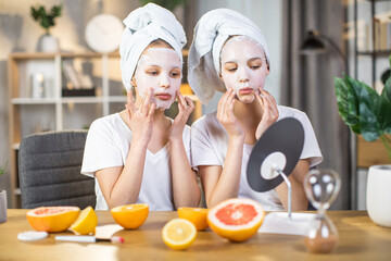 Pretty caucasian female teenagers looking at mirror and applying mask on face for hydration skin. Two sisters sending free time at or for beauty procedures. - Powered by Adobe