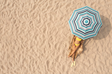 Woman resting in sunbed under striped beach umbrella at sandy coast, aerial view. Space for text