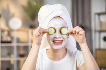 Portrait of mature woman with vitamin mask on face holding slices of cucumber on her eyes. Concept of people, skin care and spa treatment.