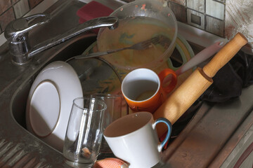 a mountain of dirty dishes accumulated in the washbasin, due to the lack of a dishwasher in the...