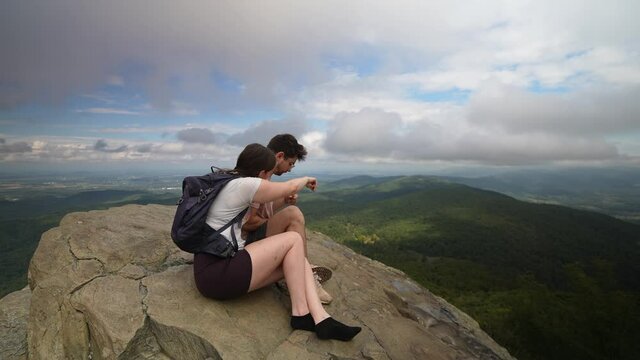 Young man and woman sitting on a rock, snacking and enjoying the beautiful view of Virginia.