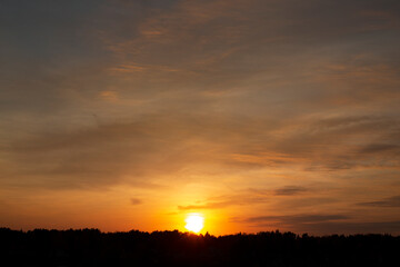 Yellow-orange, bright disc of the setting sun over a forest