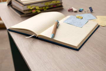 Closeup of wooden desk,opened notebook,pen,stack of books,stationary on it.Empty space.Process of...