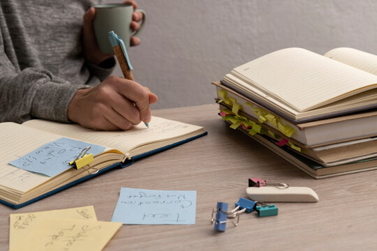 Woman writing text for commercial ads.Workplace and stack of books,papers,stationary ont, woman holding cup and pen,writing down ideas