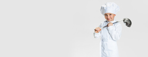 Flyer with portrait of little happy boy in white cook uniform and huge chef's hat with big ladle isolated on white studio background.