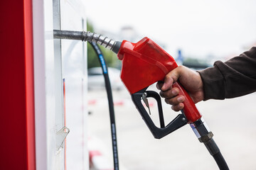 A gas station worker holds a fuel dispenser to fill the car with fuel. A young man's hand holds a...