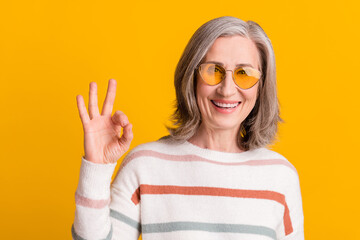 Photo of pretty sweet retired woman dressed white sweater spectacles smiling showing okey isolated yellow color background