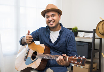 Lifestyle concept. Young asian musician playing guitar in living room at home on this weekend. Relaxing with song and music. Asian man having fun playing acoustic guitar