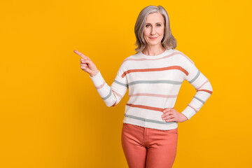 Photo of pretty adorable lady pensioner wear striped pullover pointing finger empty space smiling isolated yellow color background