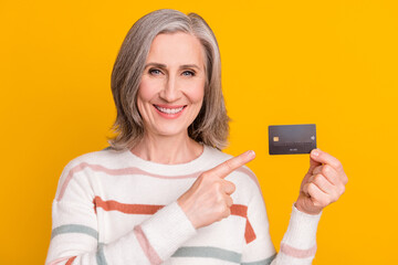 Photo of charming cute retired woman dressed white sweater smiling pointing finger debit card isolated yellow color background