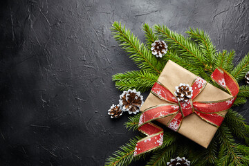 Gift box and green Christmas tree branch with cone on black background top view