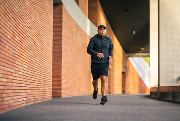 Asia man wearing jacket sportswear running on the road under the building. Young man jogging for exercise in the city. healthy lifestyle and sports concept