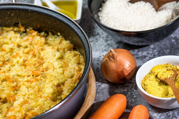 Italian vegan Risotto in a large pan with ingredients - rice, onion, carrots, spices, olive oil