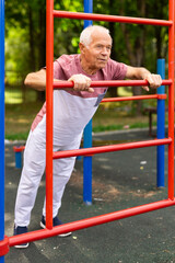 Obraz premium Sportive elderly man doing street fitness on the simulator in park