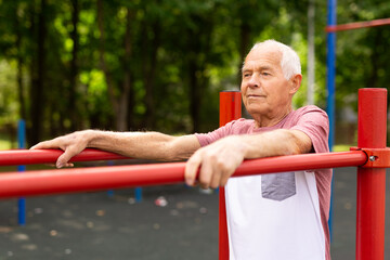 Obraz premium Elderly sportive man doing parallel bars exercise in park