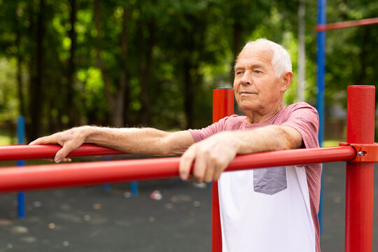 Elderly sportive man doing parallel bars exercise in park