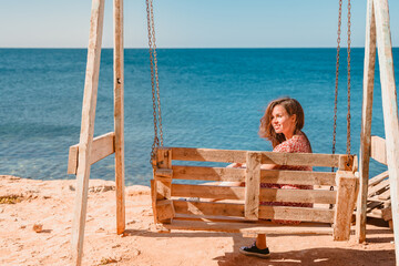 A young beautiful woman on a wooden swing on the Black Sea coast in Crimea.
