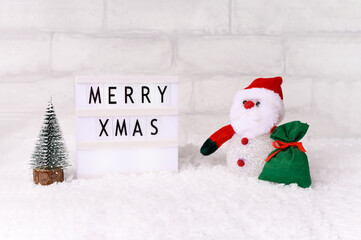 Santa Claus doll toy with miniature fir tree and gift bag on christmas time, background with snow. Front view
