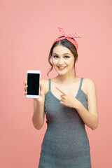 Young Asian woman point to mobile phone on pink background