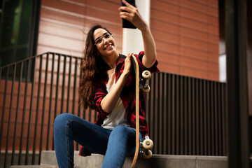 Portrait of young beautiful girl with skateboard. Happy smiling woman taking selfie photo