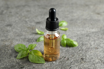 Glass bottle of basil essential oil and leaves on grey stone table