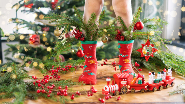 Decorated spruce branches are tucked into the socks on the feet of the child. Red Christmas train as an interior decoration. An atmospheric Christmas photo with a festive fairy mood and golden bokeh.