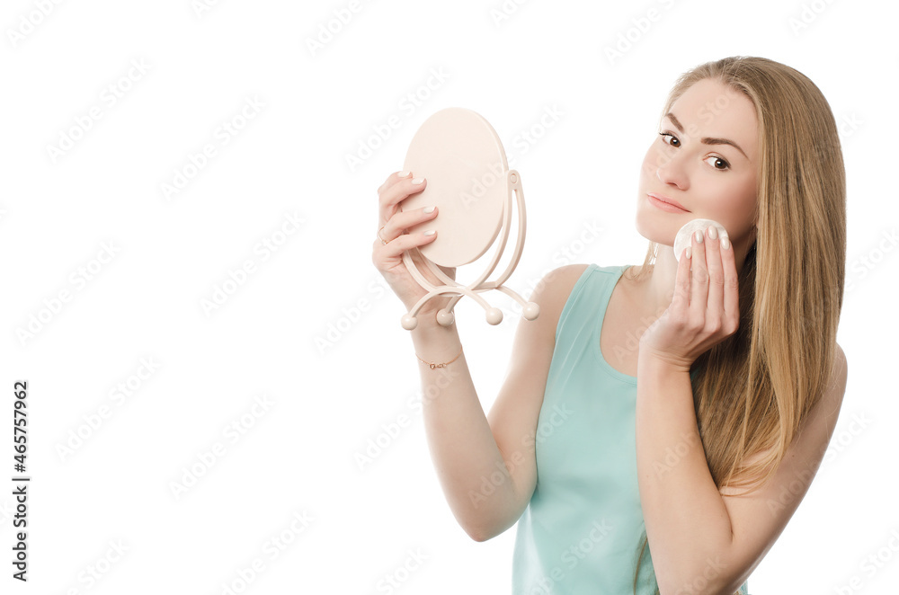 Wall mural Close-up portrait of a young woman on a white background who holds a pink mirror in her hands and wipes her face with a cotton pad