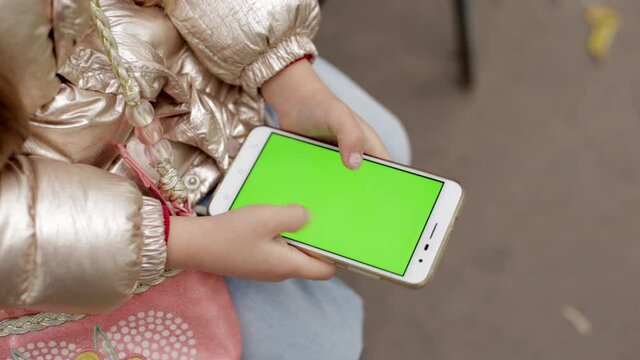 Little girl holding smartphone with green screen.