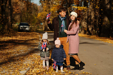 Obraz premium National holiday of United Kingdom. Family with british flags in autumn park. Britishness celebrating UK. Two kids.