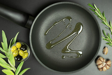 Top view of frying pan with olive oil and ingredients around it on dark background. Concept of...