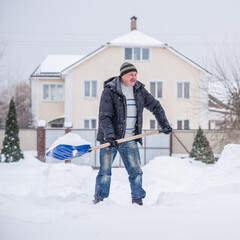 Winter, people and snow problem concept - man digging snow with shovel at yard. Man standing with blue shovel, cleaning. 