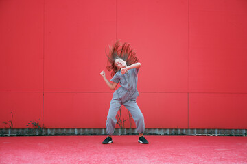 Energetic teen girl dancing waving hair outdoors by red wall. Dancer performance. Contemporary...