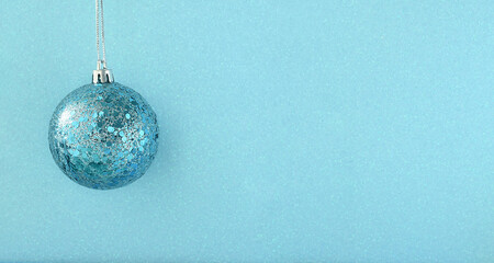 Merry Christmas and Happy New Year. Christmas blue ball hanging on a string on a shimmering shiny blue background. Greeting card or banner for website sale.