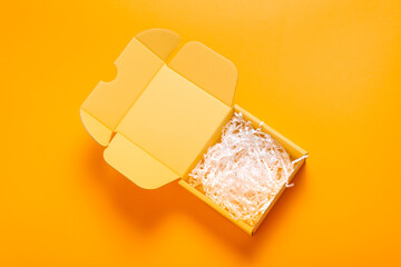 Simple yellow cardboard box on color background, empty inside with filler