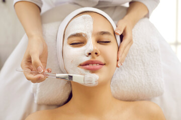 Happy beautiful young woman or teenage girl with half face covered in calming soothing pampering...